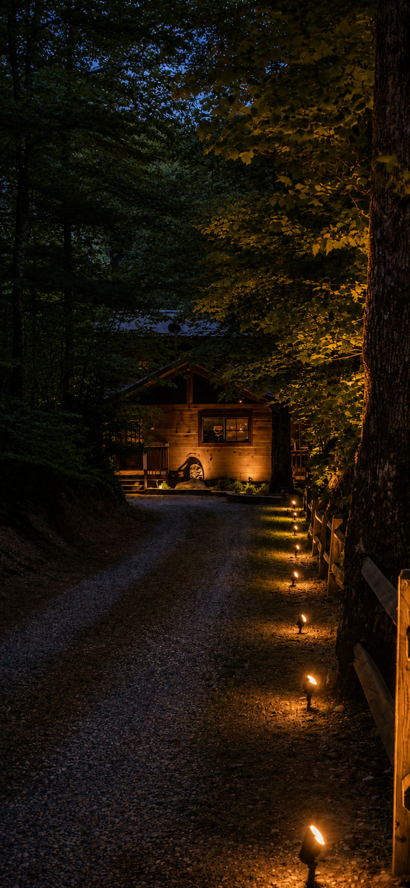 Gravel driveway approaching a warmly lit cabin among trees