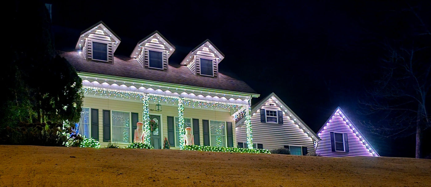 A roofline with white lights around holiday decorations at a home